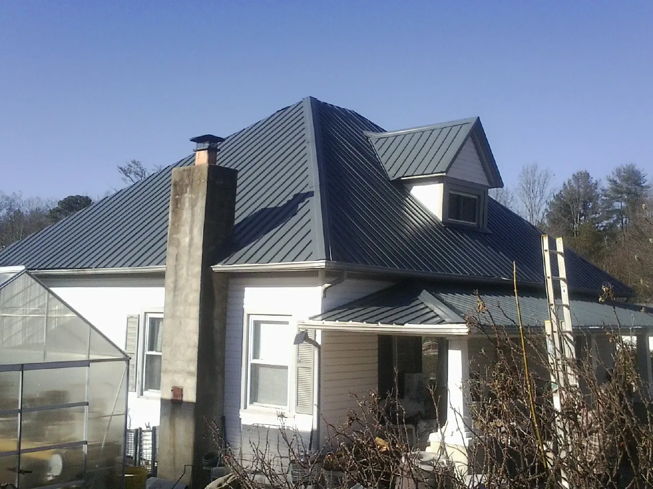 Dark blue standing seam metal roof on a white farmhouse with dormer — Slate & Tile Roof Repair by Roofing Brothers in Luke