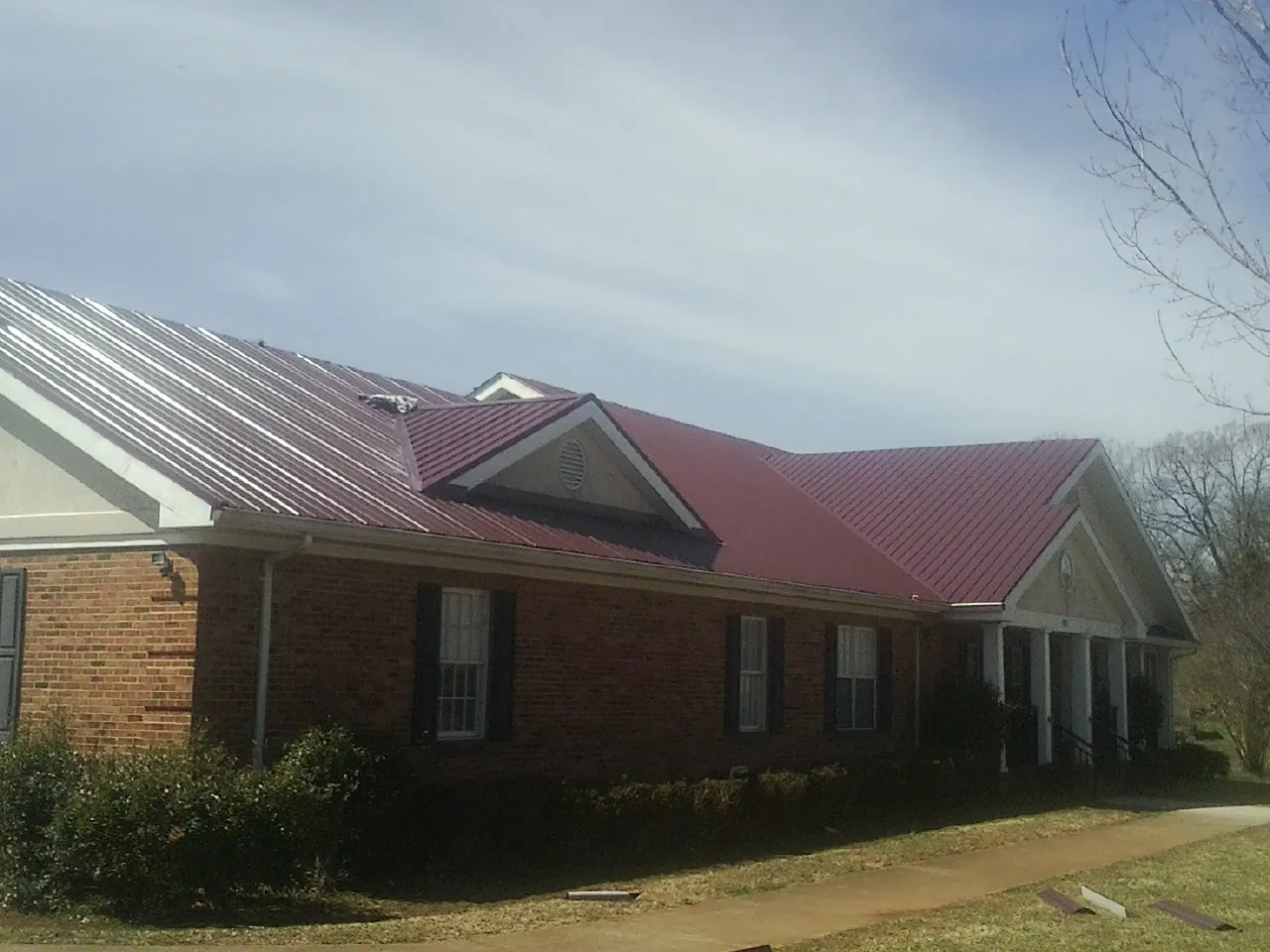 Red metal roof with gabled entries on a long brick building, from a Hail Damage Roof Repair job in Luke
