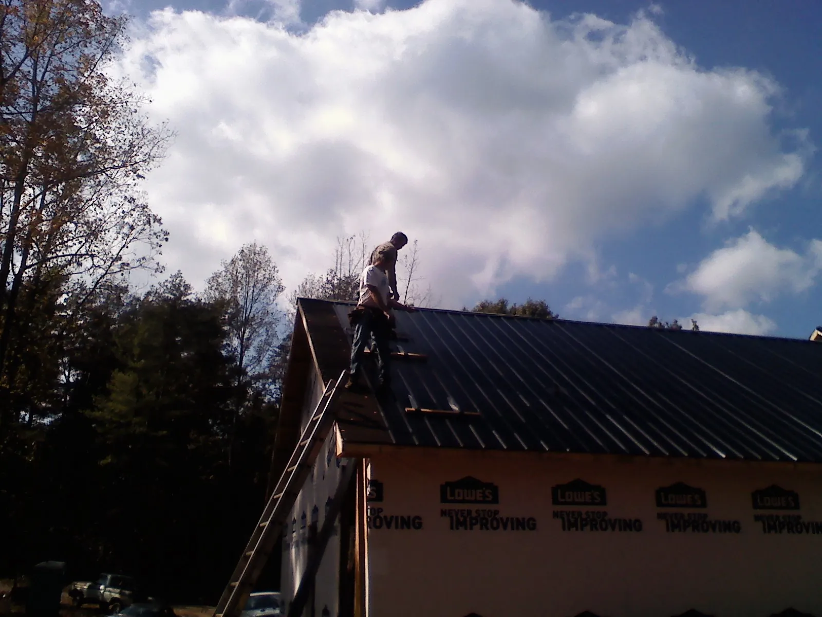 Roofer fastening dark metal panels high against a cloudy sky, from a Roof Inspection job in Luke