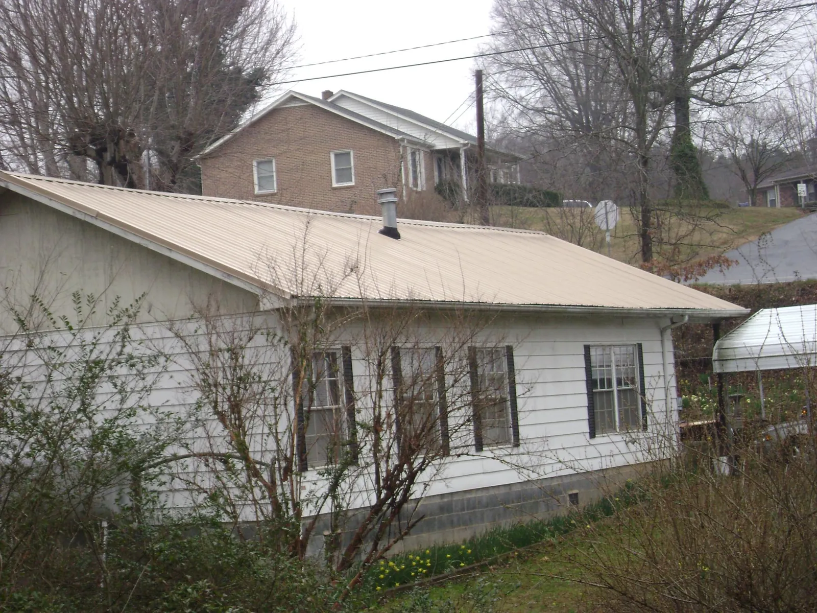 Tan metal roof on a white sided house set into a hillside — Commercial Roofing by Roofing Brothers in Luke