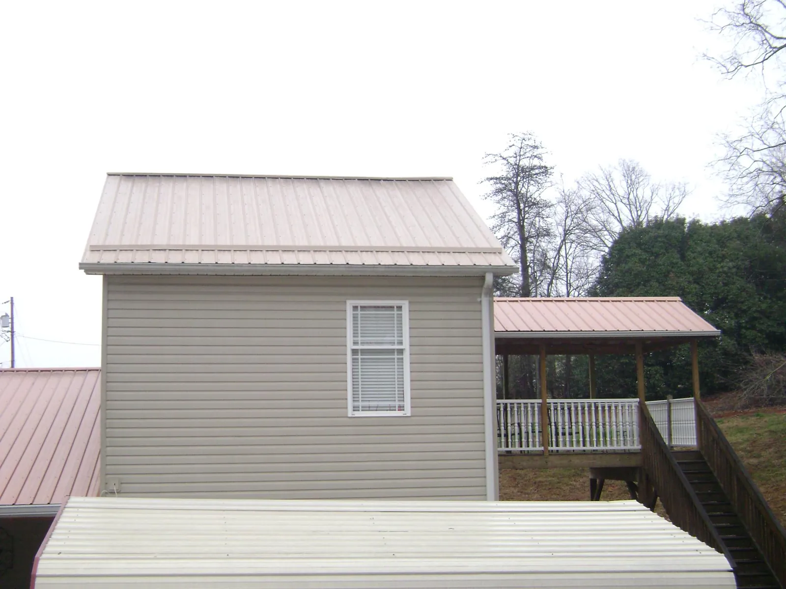 Tan metal roofs on a two story addition and attached porch, from a Roof Replacement job in Luke